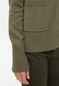 Olivgrüner Strickpullover mit einer Brusttasche, ausgestattet mit einem gerippten Saum und Bündchen. Kombiniert mit passenden olivgrünen Hosen.