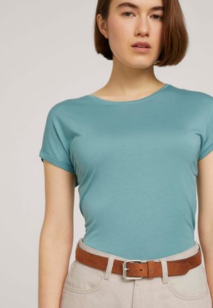 Hellblaues kurzärmliges T-Shirt aus glattem Stoff, kombiniert mit beigen Hosen und einem braunen Ledergürtel mit einer silbernen Schnalle.