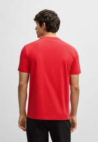 Rød T-shirt med korte ærmer lavet af bomuld, med rund hals og en glat tekstur, vist fra ryggen med et enkelt design.