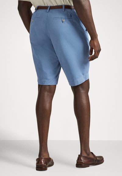 Gaiši zilas kokvilnas šorti ar taisnu griezumu, jostas cilpām, aizmugurējām kabatām un pogu aizdari. Valkāti kopā ar brūniem loaferiem.