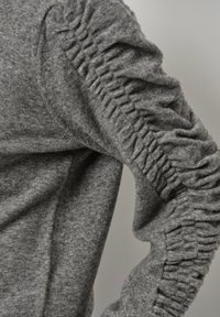 Grijze trui met gerimpelde details langs de mouwen, gemaakt van een zachte stof met een gladde textuur.