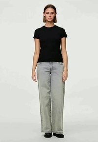 T-shirt preto com riscas, de mangas curtas, combinado com umas jeans cinzentas de perna larga de cintura alta. Calçado preto completa o visual.