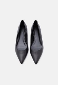 Ζευγάρι μαύρα δερμάτινα γυναικεία παπούτσια μπαλαρίνας με μυτερή μύτη και λογότυπο HUGO στην εσωτερική σόλα, απεικονισμένα από πάνω σε λευκό φόντο.