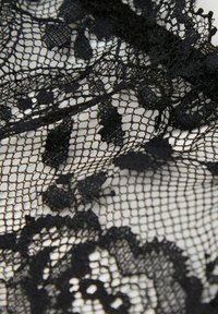 Tela de encaje negra con un intrincado diseño floral, malla fina y bordes festoneados, que muestra diversas texturas y patrones a lo largo.