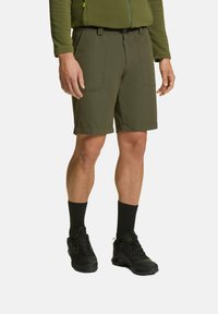 Pantaloni shorts verde scuro con una vestibilità sartoriale, dotati di due tasche frontali e orli arrotolati. Abbinati a scarpe nere e calzini.