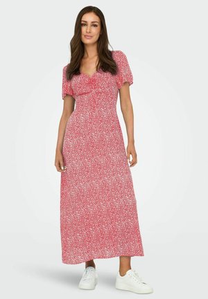 Abito maxi rosso a fiori con maniche corte a sbuffo, vita cintrata e silhouette fluida. Abbinato a scarpe da ginnastica bianche per un look casual.
