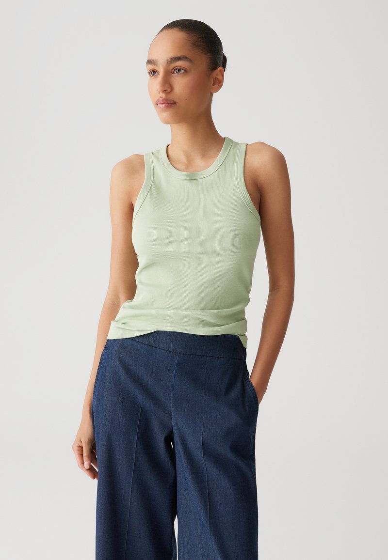 Lichtgroene geribbelde tanktop met een ronde hals en brede schouderbanden, gecombineerd met donkerblauwe wijde broekspijpen.