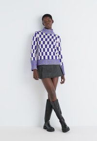 Pulover în carouri violet și alb cu guler înalt, asortat cu o fustă mini neagră și cizme negre până la genunchi. Textură netedă.