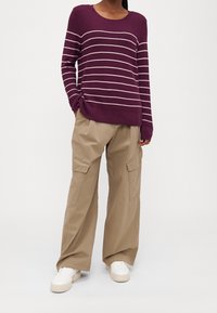 Lila stickad tröja med horisontella vita ränder, som matchas med beiga vida cargobyxor med sidofickor och en avslappnad passform.