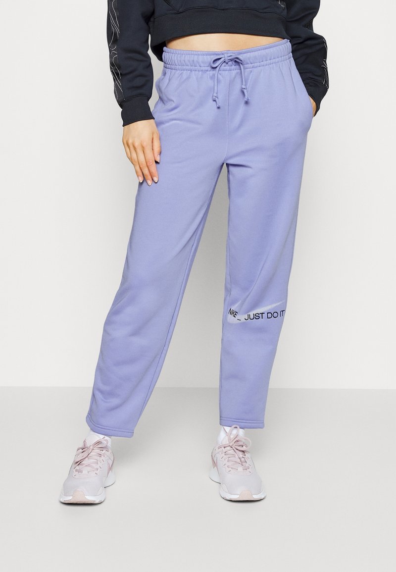 Personne portant un pantalon de jogging violet clair avec le logo "Nike Just Do It" sur la jambe gauche, un hoodie court noir et des baskets rose clair.