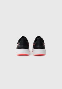 Chaussures de sport noires avec une tige en maille, une semelle blanche et des accents corail vif. Elles ont une forme arrondie et un talon texturé.
