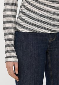 Camiseta de manga larga a rayas en blanco y negro con tejido texturizado, combinada con jeans de mezclilla azul oscuro con costuras naranjas y un corte ajustado.