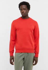 Czerwona bluza z okrągłym dekoltem, ściągaczami przy mankietach i pasie; wykonana z teksturowanej tkaniny, z małym logo na piersi.