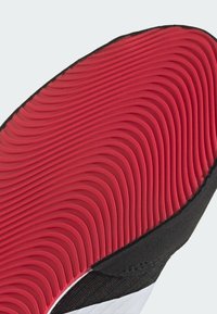 Shoe sole with a wavy, red rubber pattern, bordered by a black edge, displaying texture and depth for grip and flexibility.