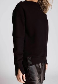 Schwarzer, übergroßer Sweatshirt aus strukturiertem Stoff, mit gerippten Bündchen und einem Logo-Patch am Saum, kombiniert mit glänzenden schwarzen Lederhosen.