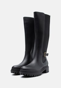 Schwarze kniehohe Lederstiefel mit groben Gummisohlen, elastischen Seitenpanelen und einer kleinen dekorativen Schnalle an der Außenseite.