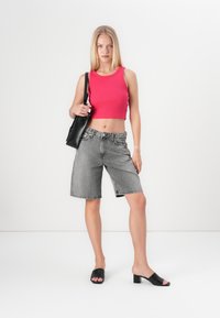 Svarte denimshorts, grå med frynset kant, parret med en lys rosa ribbet crop-top. Svarte åpne tå blokkhæl mules og en svart skulderveske.