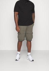 Černé polo triko, khaki cargo šortky s několika kapsami a bílé tenisky s modrými akcenty. Neformální oblečení s krátkými rukávy a ohrnutými lemy.