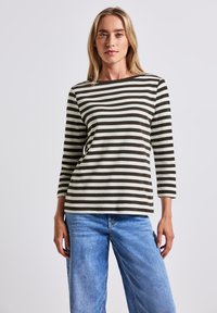 Grünes und cremefarbenes gestreiftes Langarmoberteil mit einem Schiffsausschnitt, aus leichtem Stoff, kombiniert mit blauen Jeans.