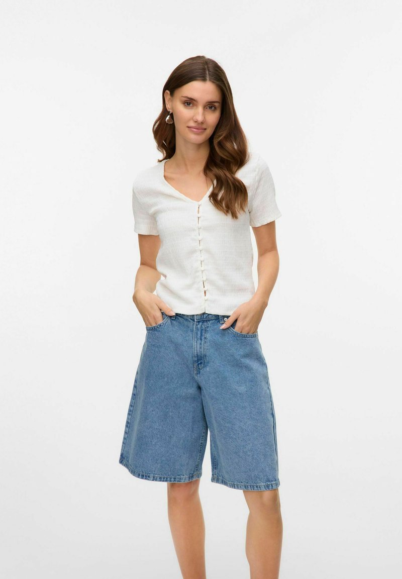 Blusa bianca a maniche corte con colletto a V in tessuto testurizzato abbinata a pantaloni corti in denim blu, con una vestibilità ampia e tasche.
