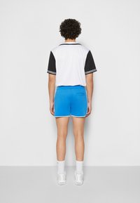 Hvit og svart kortermet skjorte med svart krage, kombinert med blå treningsshorts med baklomme og hvite detaljer. Hvite joggesko.