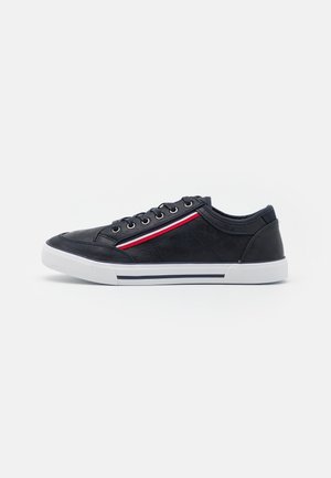 Schwarzer Sneaker mit niedrigem Schaft, weißer Sohle, schwarzen Schnürsenkeln und roten, weißen und blauen Streifen an der Seite, von der Außenseite gezeigt.