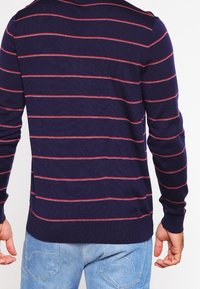 Pull-over bleu marine à rayures rouges horizontales, confectionné en tissu doux. Présente un col rond ainsi que des poignets et un ourlet côtelés.