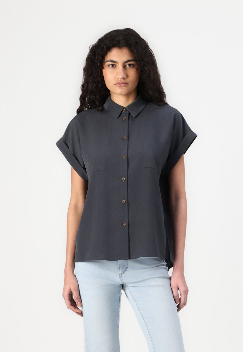 Camisa de manga curta cinza escuro com botão na frente, dois bolsos no peito e mangas com a bainha arregaçada. Textura suave e corte relaxado.