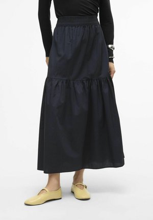 Gonna midi a balze blu navy con cintura elastica; tessuto leggero con una texture liscia. Abbinata a scarpe piatte gialle, minimaliste.