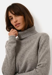 Grå polotröja i mjukt tyg med ribbad krage och muddar, figursydd design med slät textur och minimal detaljering.