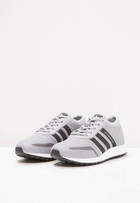 Grå sportskor med mesh-överdela, svarta randdetaljer och vit sula. Har snörningsdesign och vadderad krage för komfort.