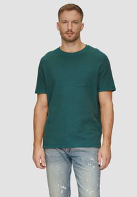 Türkisfarbene Baumwoll-T-Shirt mit Rundhalsausschnitt, kurzen Ärmeln und einer Brusttasche. Verfügt über eine strukturierte Oberfläche und eine lässige Passform. Trägt es mit ausgewaschenen blauen Jeans.