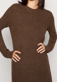 Pull marron tricoté avec un col rond et des manches longues, présentant une texture côtelée et une coupe ajustée. Matière douce et confortable.