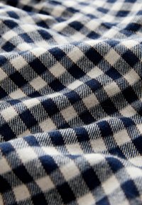 Kockovaný textil s striedajúcimi sa námornícky modrými a krémovými štvorcami, s jemnou textúrou a mierne rozstrapkanými okrajmi v teplom, útulnom vzore.