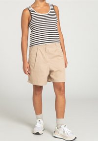 Béžové bavlněné kraťasy s předními sklady, spárované s černobílým pruhovaným tílkem. Doplněné o světle barevné tenisky a šedé ponožky.