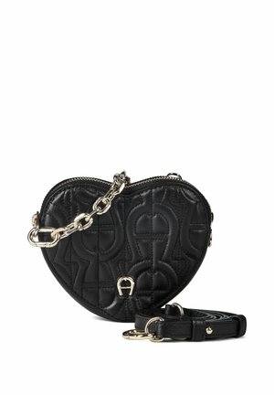 Sac à main en cuir matelassé noir en forme de cœur avec détail chaîne dorée et bandoulière amovible sur fond blanc.