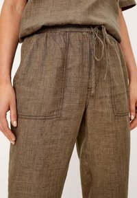 Bruine linnen broek met een ontspannen pasvorm, voorzien van een elastische tailleband, trekkoord en twee voorste zakken. Fijn textuurpatroon over de gehele broek.