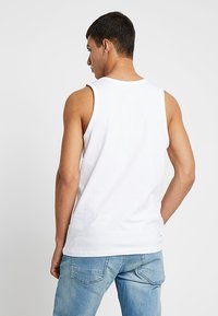 Fehér pamut ujjatlan felső kerek nyakkivágással és széles karvégekkel. A háta sima, látható varrással, világoskék farmerral párosítva.