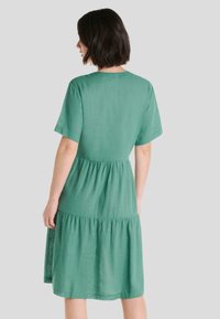 Vestido verde de manga corta hecho de lino, con un corsé ajustado y una falda acampanada en capas, que presenta una textura suave y un caído natural.