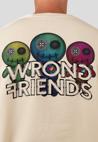 Felpa beige con tre figure in stile cartone animato nei colori verde, blu e viola, e la scritta "WRONG FRIENDS" in grassetto e nero.