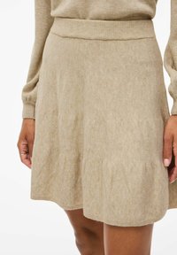 Gonna di maglia beige con vita a coste, forma svasata e texture liscia. L'orlo è leggermente curvato, offrendo una vestibilità rilassata.