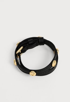 Black leather bracelet with gold round studs and a gold buckle, shown coiled in a circle on a plain white background.