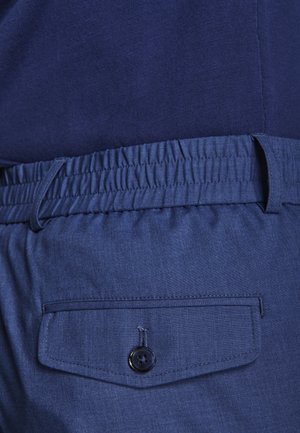 Primo piano di pantaloni con vita elastica blu e tasca posteriore con bottone, indossati con una maglietta blu navy.