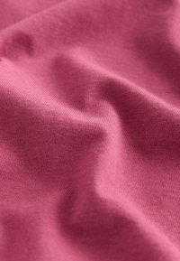 Približek mehke, teksturirane roza tkanine z vidnim finim vzorcem pletenja in nežnimi gubami, ki ustvarjajo sence in poudarke.