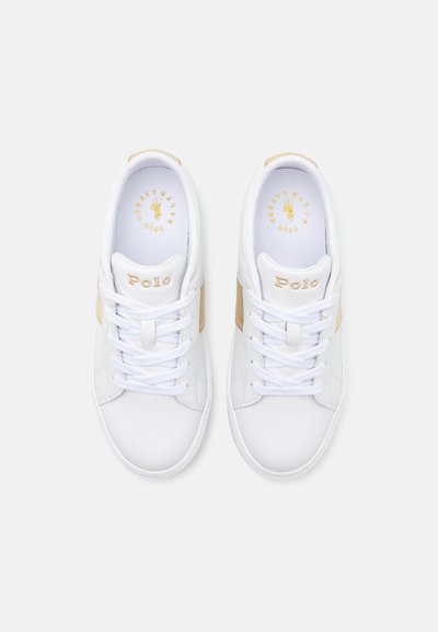Vita sneakers med en slät läderöverdel, ljusbruna detaljer, rund tå, platta snören, och "Polo"-logotyp i guld på tungan.