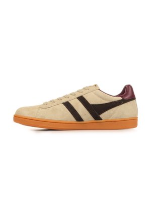 Low-top beige suède sneaker met gumzool, donkerbruine zijstrepen en bordeaux rode hielkraag, gezien vanaf de buitenkant.