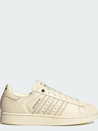 Λευκό αθλητικό παπούτσι Adidas Superstar με μύτη κέλυφος, τρεις διάτρητες ρίγες, σήμανση "SUPERSTAR" και λευκά κορδόνια.