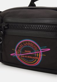 Borsa in tessuto nero con una zip prominente, caratterizzata da un logo circolare colorato con la scritta "Karl Lagerfeld" e "Paris" in colori vivaci.