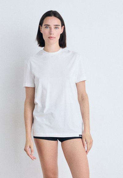 Weißes Baumwoll-T-Shirt mit Rundhalsausschnitt und kurzen Ärmeln, lässiger Schnitt. Getragen mit schwarzen Shorts. Glatte Textur, minimalistisches Design.