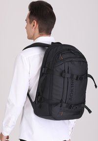 Zaino nero realizzato in tessuto texturizzato, caratterizzato da spallacci regolabili, numerose cerniere e un pannello posteriore imbottito per il comfort.